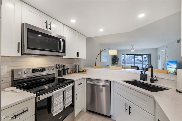 kitchen with white cabinetry, stainless steel appliances, sink, ceiling fan, and light stone counters