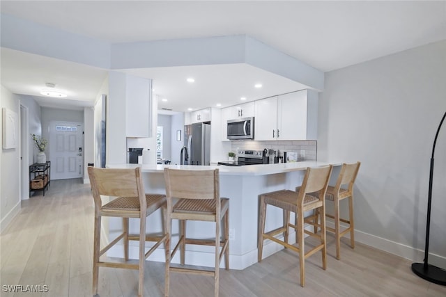 kitchen with kitchen peninsula, a kitchen bar, white cabinetry, light hardwood / wood-style flooring, and stainless steel appliances