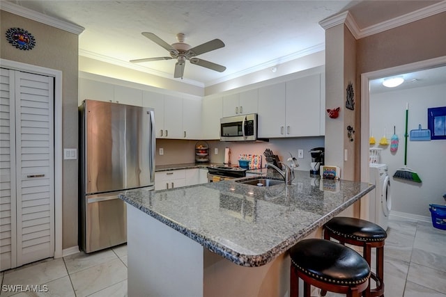 kitchen with a breakfast bar, sink, appliances with stainless steel finishes, kitchen peninsula, and washer and clothes dryer