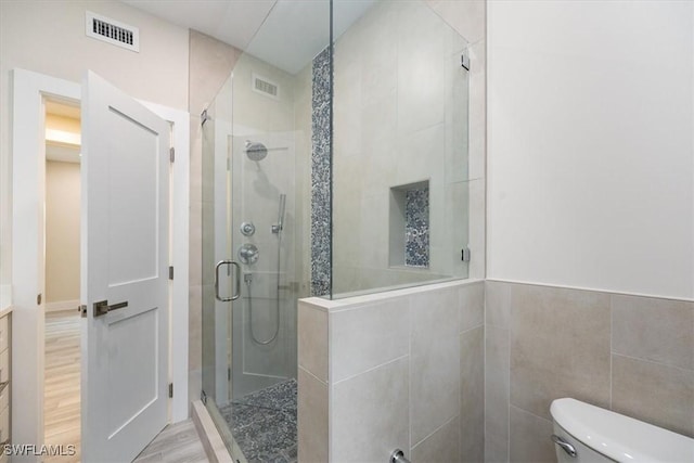 full bath with tile walls, visible vents, toilet, a stall shower, and wood finished floors