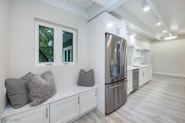 kitchen featuring beamed ceiling, stainless steel appliances, light countertops, white cabinetry, and a sink