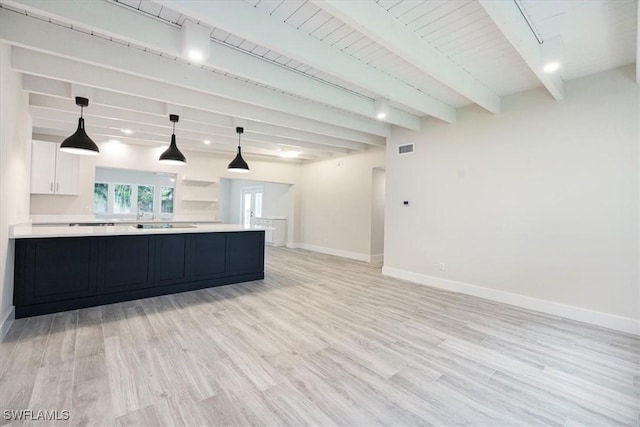 kitchen with beam ceiling, light countertops, open floor plan, white cabinetry, and baseboards