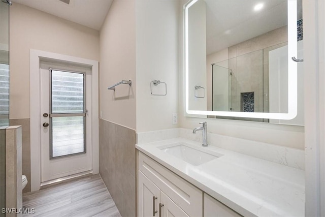 bathroom with a wainscoted wall, tile walls, toilet, a stall shower, and vanity