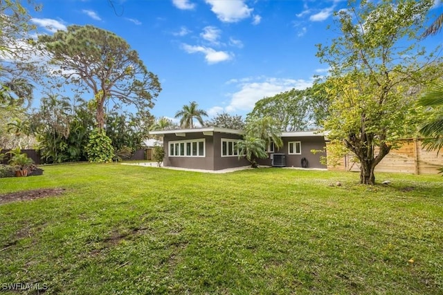 back of property featuring fence, central AC unit, a lawn, and stucco siding