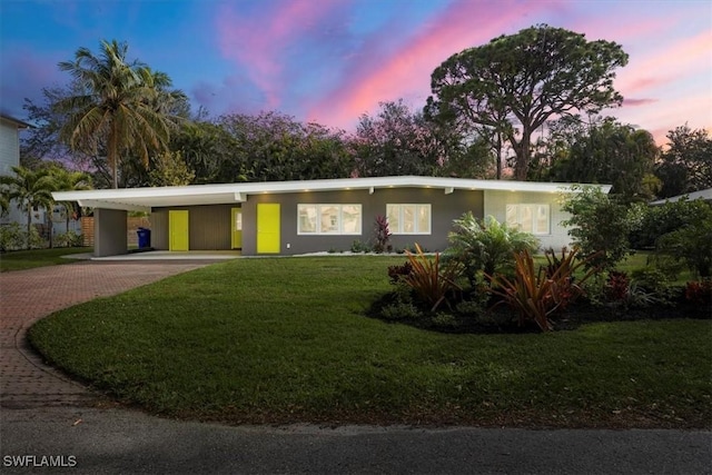 mid-century home featuring an attached carport, decorative driveway, a lawn, and stucco siding