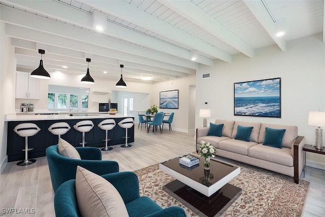 living room with visible vents, light wood-style flooring, beam ceiling, and baseboards