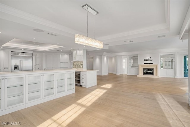 kitchen featuring a tray ceiling, beverage cooler, hanging light fixtures, a kitchen island, and stainless steel built in refrigerator