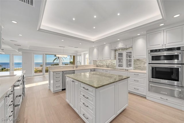 kitchen with a raised ceiling, kitchen peninsula, appliances with stainless steel finishes, and a center island