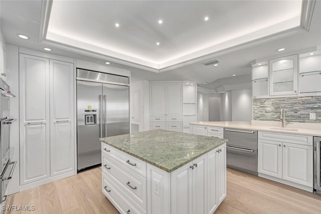 kitchen featuring a tray ceiling, sink, built in fridge, white cabinets, and a center island