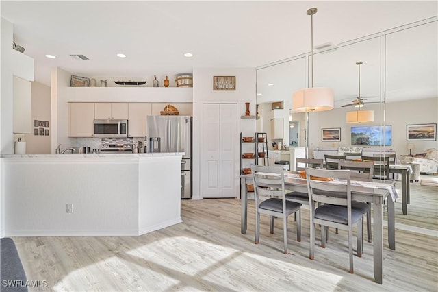 kitchen with tasteful backsplash, white cabinetry, hanging light fixtures, light wood-type flooring, and appliances with stainless steel finishes