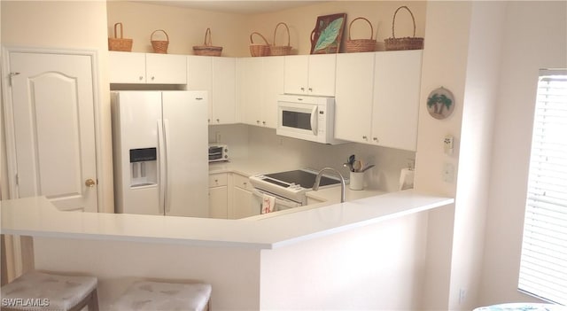 kitchen with white appliances, white cabinets, a healthy amount of sunlight, kitchen peninsula, and a breakfast bar area