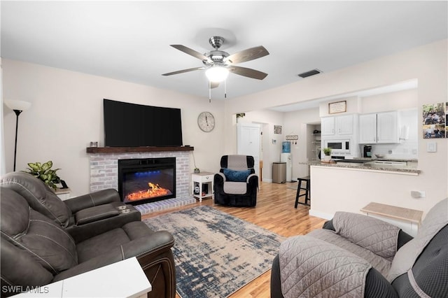 living area with a brick fireplace, light wood-style flooring, visible vents, and ceiling fan