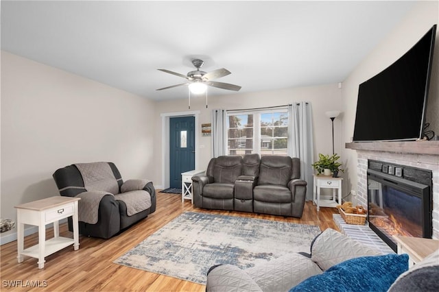 living room featuring a fireplace, ceiling fan, and light wood-type flooring