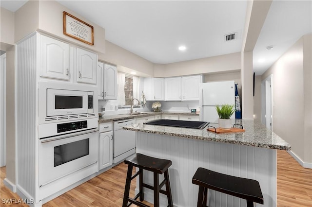 kitchen featuring white appliances, a kitchen island, white cabinetry, light hardwood / wood-style floors, and sink