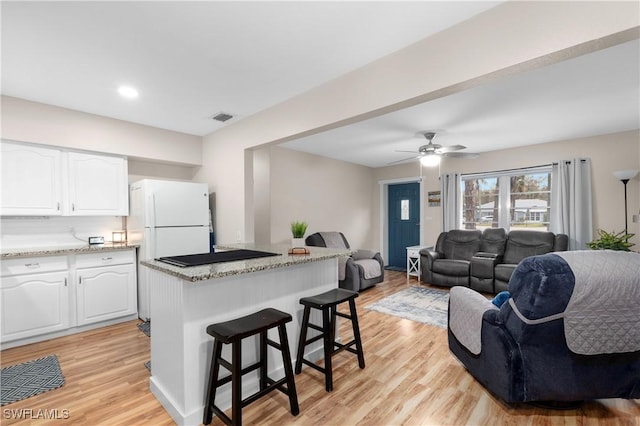 kitchen featuring light stone countertops, a kitchen breakfast bar, white cabinets, and light wood-type flooring