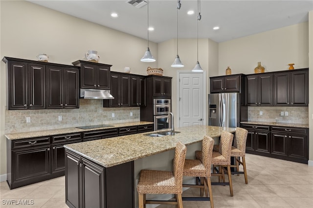 kitchen with appliances with stainless steel finishes, a breakfast bar, an island with sink, sink, and hanging light fixtures