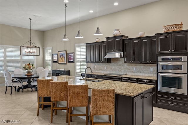 kitchen featuring a center island with sink, stainless steel double oven, black electric stovetop, a breakfast bar, and sink