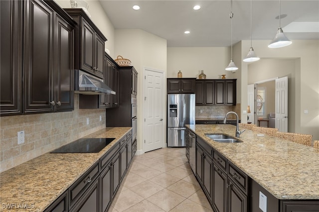 kitchen featuring a center island with sink, sink, light stone counters, decorative light fixtures, and stainless steel appliances