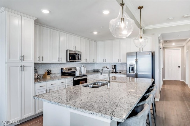 kitchen with pendant lighting, sink, appliances with stainless steel finishes, white cabinets, and a center island with sink