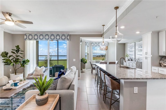 kitchen with pendant lighting, sink, white cabinets, a kitchen bar, and light stone countertops