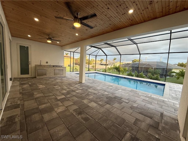 view of pool featuring a lanai, a patio area, ceiling fan, and an outdoor kitchen