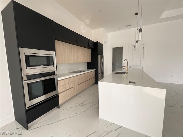 kitchen with sink, appliances with stainless steel finishes, an island with sink, decorative light fixtures, and light brown cabinets