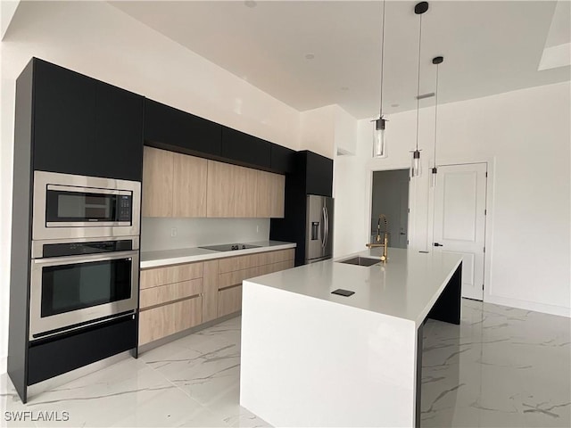 kitchen featuring appliances with stainless steel finishes, light brown cabinetry, an island with sink, sink, and hanging light fixtures