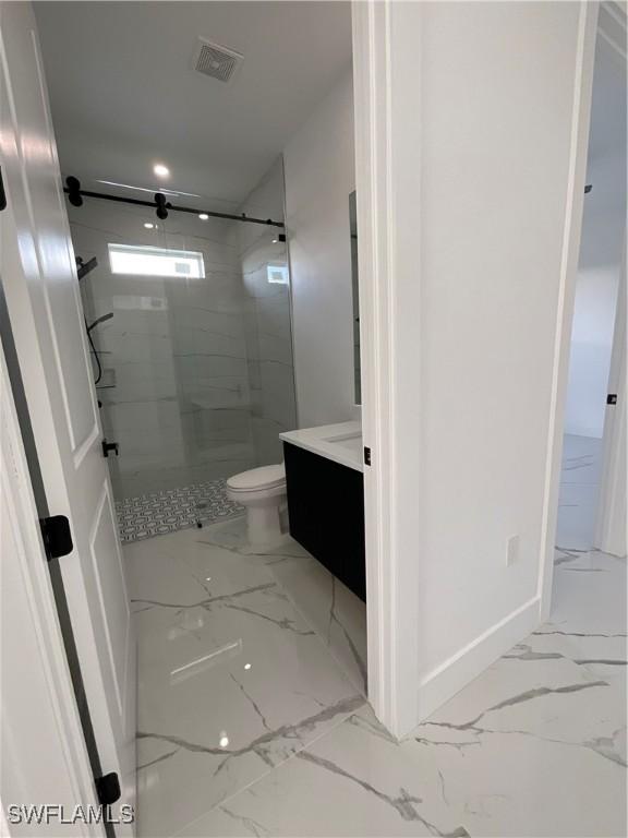 bathroom with a tile shower, vanity, and toilet