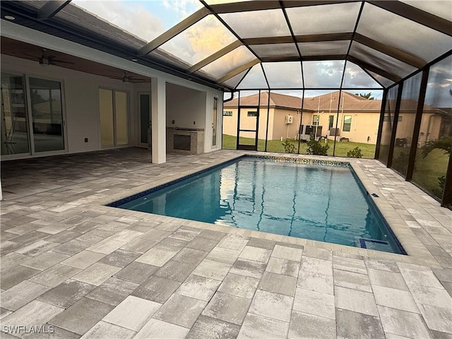 view of pool featuring an outdoor kitchen, a patio area, ceiling fan, and glass enclosure