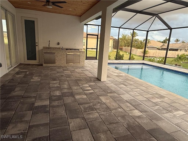 view of swimming pool featuring ceiling fan, a patio, glass enclosure, and exterior kitchen