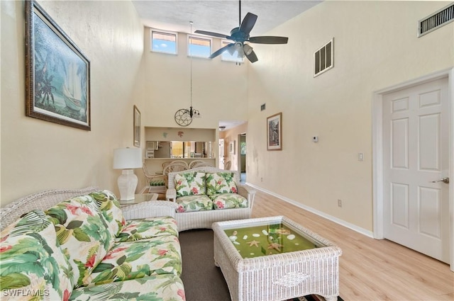 living room with light hardwood / wood-style floors, a towering ceiling, and ceiling fan