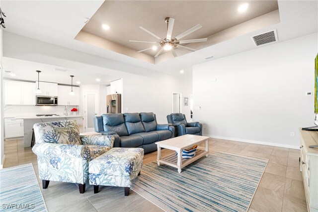 living room featuring ceiling fan, light tile patterned flooring, and a tray ceiling