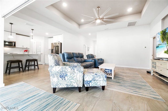 living room featuring ceiling fan and a raised ceiling