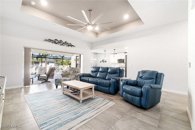 tiled living room with ceiling fan and a tray ceiling