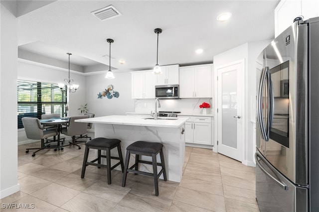 kitchen with white cabinetry, stainless steel appliances, an island with sink, sink, and hanging light fixtures