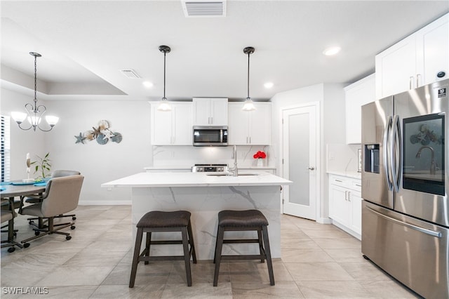 kitchen with decorative light fixtures, white cabinets, appliances with stainless steel finishes, and a center island with sink