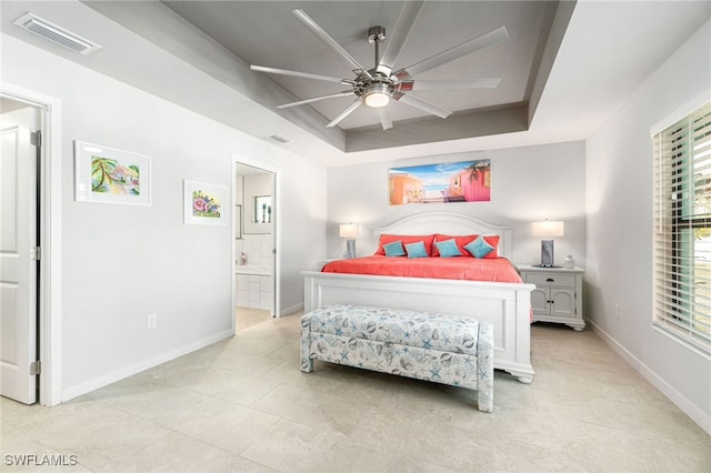 bedroom with ceiling fan, a raised ceiling, and ensuite bath