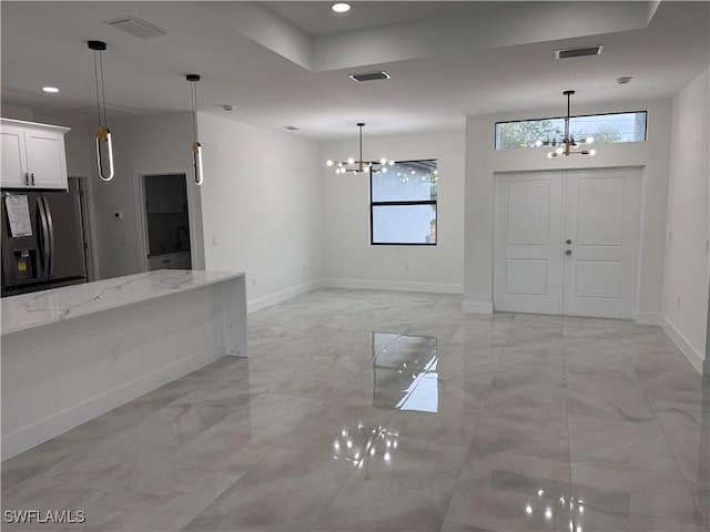 kitchen with black fridge with ice dispenser, white cabinetry, light stone counters, and an inviting chandelier