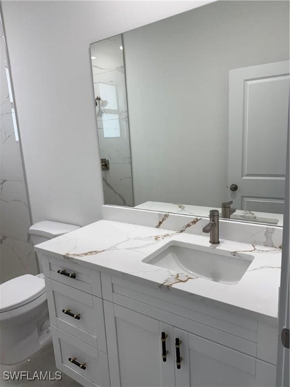 bathroom with toilet, a tile shower, and vanity