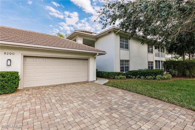 view of front of home with a garage, a tile roof, decorative driveway, stucco siding, and a front lawn