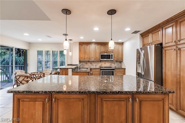 kitchen featuring visible vents, dark stone countertops, a kitchen island with sink, stainless steel appliances, and backsplash