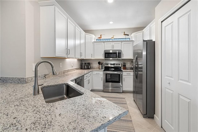 kitchen with light stone countertops, white cabinetry, stainless steel appliances, sink, and kitchen peninsula