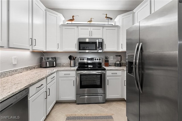 kitchen featuring light tile patterned floors, appliances with stainless steel finishes, white cabinets, and light stone counters