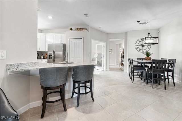 kitchen with decorative light fixtures, kitchen peninsula, stainless steel refrigerator with ice dispenser, a kitchen bar, and white cabinets