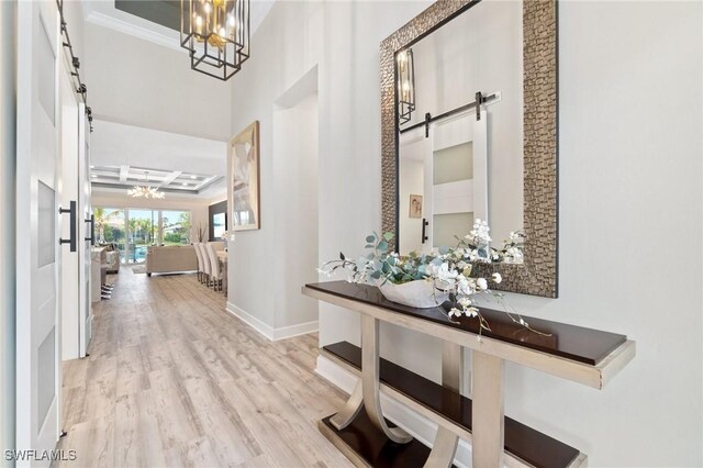 hallway featuring an inviting chandelier, a barn door, light hardwood / wood-style floors, and crown molding