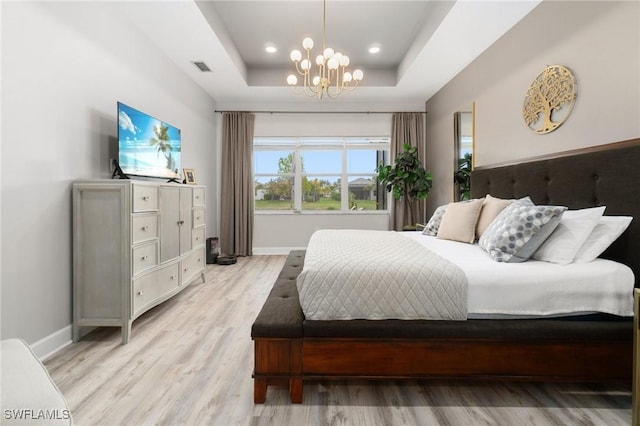 bedroom featuring a chandelier, light wood-type flooring, and a tray ceiling