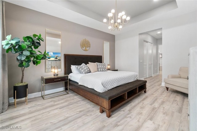 bedroom with a chandelier, a raised ceiling, baseboards, and wood finished floors