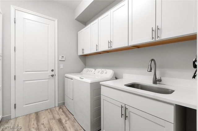 clothes washing area with washer and dryer, cabinet space, a sink, and light wood-style flooring