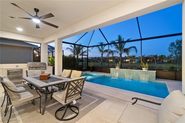 pool at dusk with an outdoor kitchen, a patio area, grilling area, glass enclosure, and ceiling fan