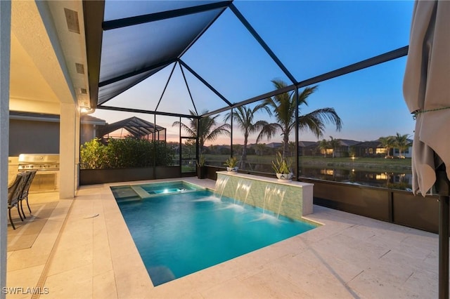 pool at dusk featuring pool water feature, an outdoor kitchen, a water view, area for grilling, and glass enclosure